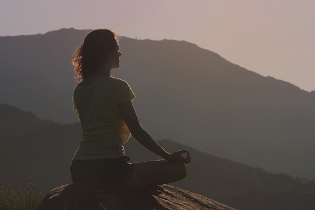 Woman Sitting On The Rock And Meditating In Yoga Pose. Back View